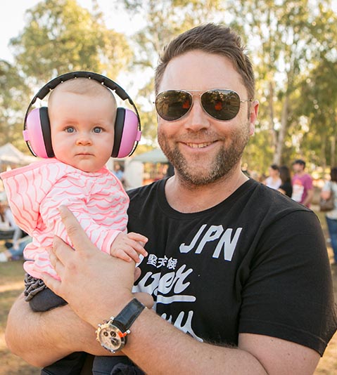 Father holding young child with headphones on at a music event, Packer Park, Carnegie